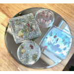 Four glittery resin coasters with embedded dried flowers on a round tray