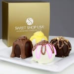 Assorted gourmet chocolate truffles on a white plate with a gold gift box