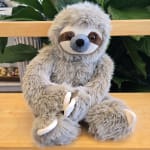 Plush sloth toy sitting on a wooden bench