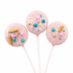 Three pink cake pops with colorful sprinkles on white sticks