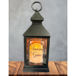 Black metal lantern with glass panel featuring 'Amazing Grace' text and warm orange glow
