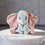 Blue plush elephant with pink ears sitting on a marble surface