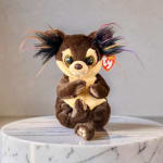 Small plush animal with rainbow-tipped ears sitting on a marble pedestal