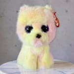 Pastel plush teddy bear with large eyes and a red tag