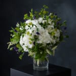 White hydrangea bouquet with purple bell-shaped flowers in a clear glass vase