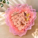 Heart-shaped bouquet of peach roses wrapped in pink paper with butterfly decorations