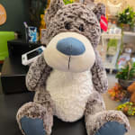 Large plush teddy bear sitting on a counter in a flower shop