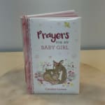 A pink children's book titled "Prayers for My Baby Girl" stands upright on a table.