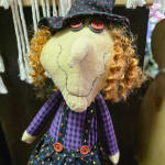 A handmade witch doll with a black hat and purple plaid outfit