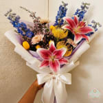 Handheld bouquet of yellow tulips and pale flowers wrapped in lavender and white paper