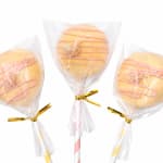 Three wrapped cake pops with pink drizzle on sticks