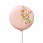 Pink cake pop topped with colorful sprinkles on a white stick