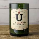 Green glass jar candle with cream label reading Unwined Candle Co. on a wooden surface