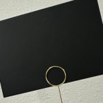 Black card with a gold ring pick on a textured surface