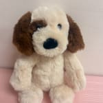 Plush dog toy with cream and brown fur sitting against a pale wall