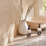 White vase with dried grasses beside two pump bottles on a countertop