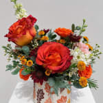 Orange and red roses arranged in a patterned vase with small accent flowers