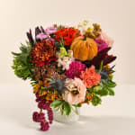 Autumn bouquet with mixed flowers and a small pumpkin in a clear glass vase