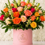Mixed roses and lilies arranged in a pink hatbox.