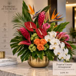 Tropical flower arrangement in a gold vase with orchids, anthuriums, and orange roses
