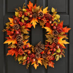 Autumn wreath with orange leaves, berries, and pinecones on a dark door