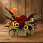 Mixed bouquet of red roses, orange gerbera daisies, and purple blooms in a wooden box