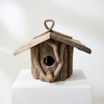 Rustic wooden birdhouse made from driftwood on a white pedestal