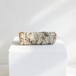 A bundled sage smudge stick rests on a white pedestal.
