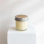 Glass jar candle with a metal lid on a white pedestal