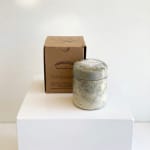 A candle jar with a cardboard box on a white pedestal