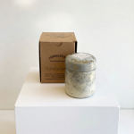 A small candle jar with a cardboard box on a white pedestal