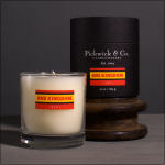 Two labeled candles, one in a glass tumbler and one in a black tin box