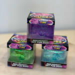Three glittery dough cubes in colorful boxes stacked on a table