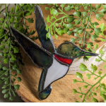 Stained glass hummingbird ornament among green fern-like foliage
