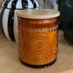 Amber glass candle jar with a wooden lid on a table