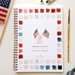 Watercolor workbook with small American flags and a paintbrush on a white surface