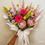 Handheld bouquet of yellow flowers wrapped in blue and white paper with a white ribbon