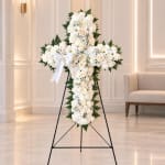 White floral cross on a black stand with a ribbon bow