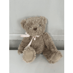 Plush teddy bear with a pink ribbon bow sitting against a wall