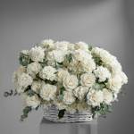 White rose arrangement in a white wicker basket with eucalyptus accents