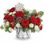 Red roses and white flowers arranged in a clear glass vase with pinecones
