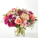 Mixed bouquet of pink, peach, and purple flowers in a clear glass vase