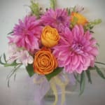 Pink and orange mixed flowers arranged in a clear vase with ribbon