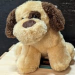 Plush dog toy with tan and brown fur sitting on a wooden surface