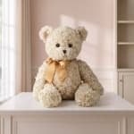 Cream teddy bear with a gold ribbon sitting on a table