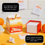 Orange juice carton-shaped note pad with loose paper sheets and a pencil