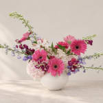 Pink gerbera daisies and mixed blooms in a white vase
