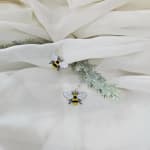White fabric with two bee-shaped dangling earrings and faux greenery