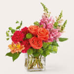 Mixed bouquet of orange roses, pink snapdragons, and red carnations in a glass vase