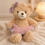 Plush teddy bear with a pink tutu and bow sitting on a blanket